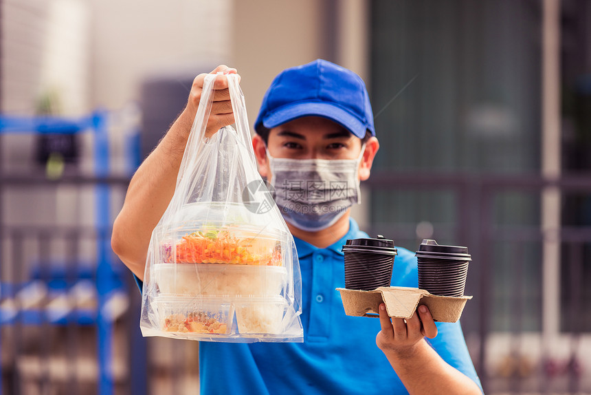 身着蓝制服的亚洲青年送货员戴面罩提供杂货服务根据流行冠状在前屋提供大米食品盒塑料袋和咖啡回到新的正常概念图片