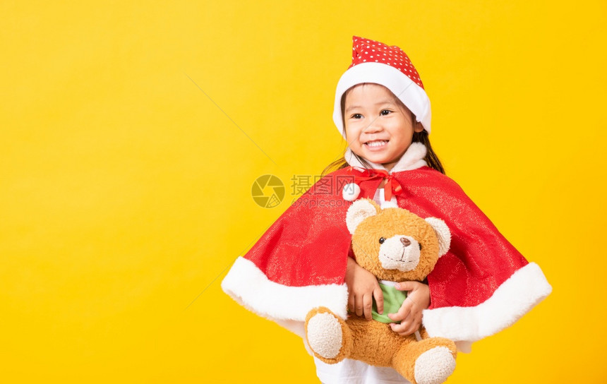 穿着圣诞老人帽子的小孩穿着圣诞帽子的小孩亚洲可爱女孩的肖像微笑着拥抱的泰迪熊圣诞日的概念图片