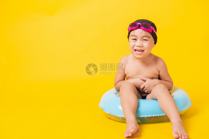 暑假概念肖莱特亚洲快乐可爱的小男孩穿着护目镜泳衣握着海滩蓝色充气环基德玩得开心坐在充气机里工作室拍着孤立的黄色背景图片