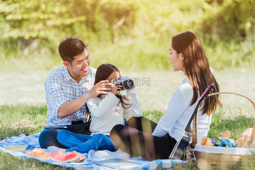 快乐的亚洲年轻家庭父亲母和小女儿快乐享受户外野餐一起坐在毯子上图片