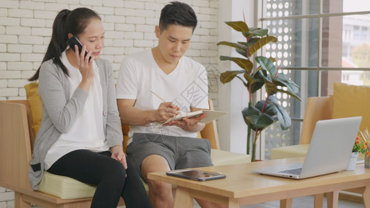 亚洲幸福家庭夫妇妻工作确认订票通过谈话电交并一起在家中客厅写信息笔记图片