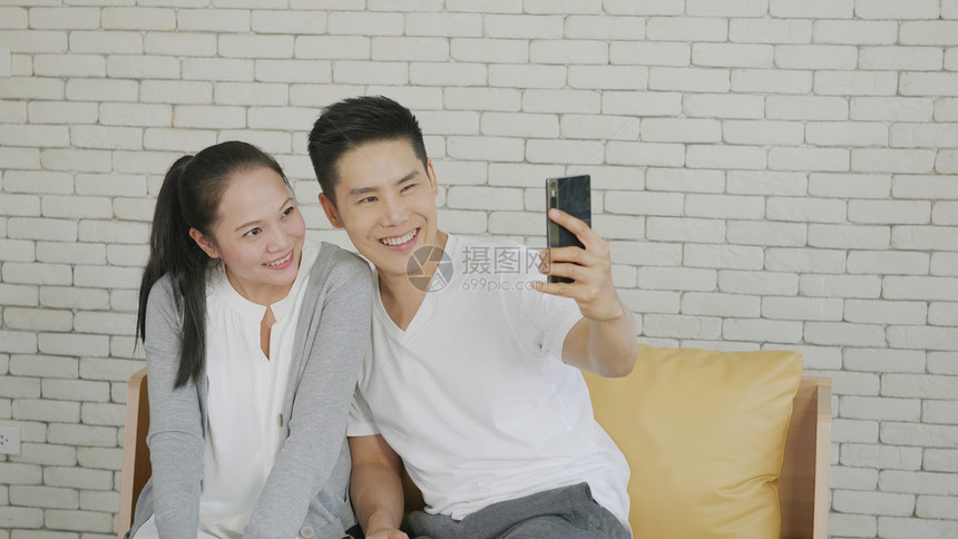 幸福的亚洲美满家庭夫妇夫妻笑着坐在客厅沙发上用智能手机自拍男女朋友在家放松图片