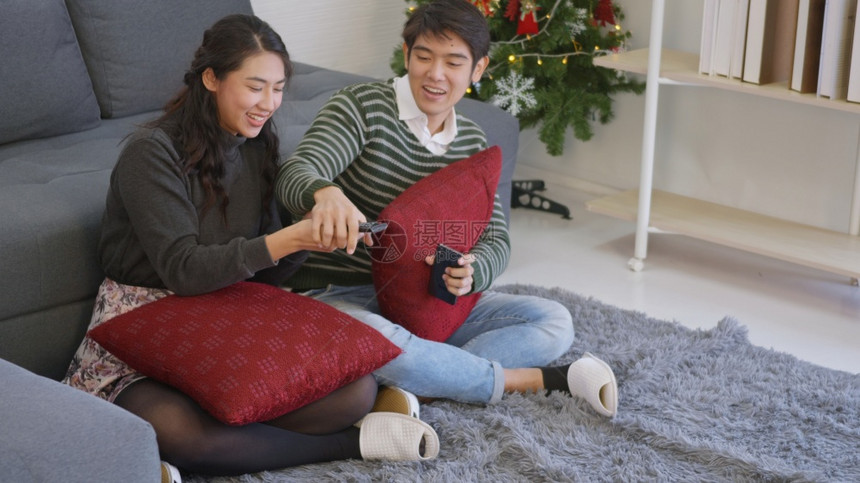 快乐的亚洲美丽年轻夫妇家庭快乐妻妇在寒冬日一起家客厅过冬一起看电视娱乐或影并努力争取遥控图片