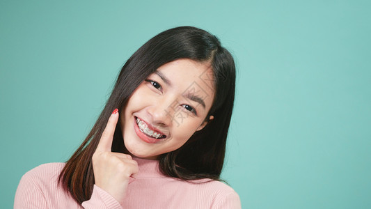青春的亚洲年轻美女微笑着在蓝色背景孤立的牙齿上佩戴硅酮或口服牙膏用可移动的牙套后保留工具背景图片