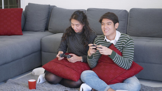 快乐的亚洲美丽的年轻家庭夫妇夫妻笑嘻嘻的玩着游戏机拿着游戏机快乐和游戏的概念背景