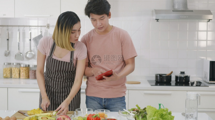 幸福的亚洲美丽年轻夫妇在家中厨房一起烹饪蔬菜沙拉男人和女在网上烹饪课用笔记本电脑做食谱图片
