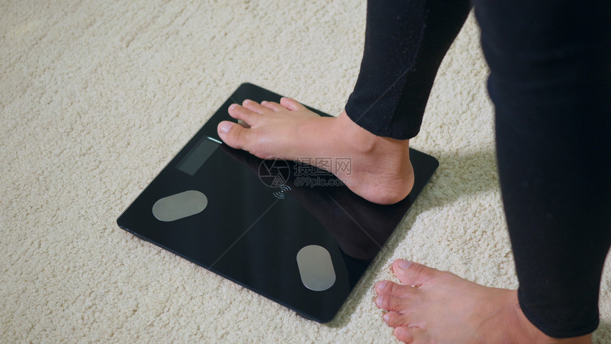 亚洲青年女子腿脚站在电压地板上女在家工作起居室女站在数字称重机上健康减控制概念慢动作图片