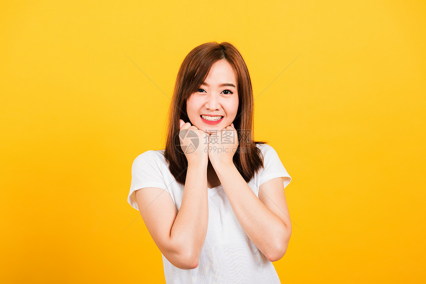 亚洲快乐的肖像亚洲美丽可爱的年轻女子站着穿T恤短袖快乐的拳头紧按在下巴图片