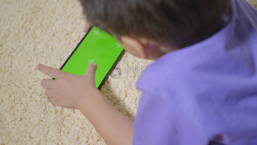 亚洲男孩学龄前在家中移动电话上玩子游戏数码小孩手持智能机绿色屏幕使用和持有智能手机绿色屏幕技术创造概念图片