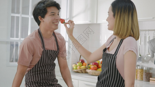 女将草莓放在男人的鼻子上在家里的厨房共度时间图片