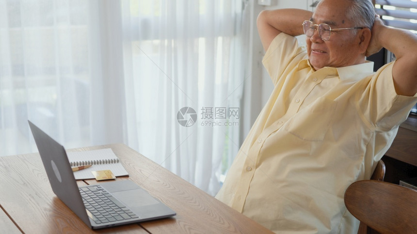 在家客厅用笔记本电脑工作时坐在椅子上工作时戴眼镜的老人快乐老人用电脑退休老人祖父在家工作图片