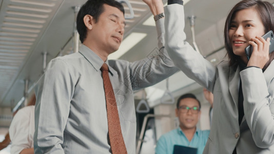 早上班时站在地铁列车上的男女商人和使用手机打电话人交通概念图片