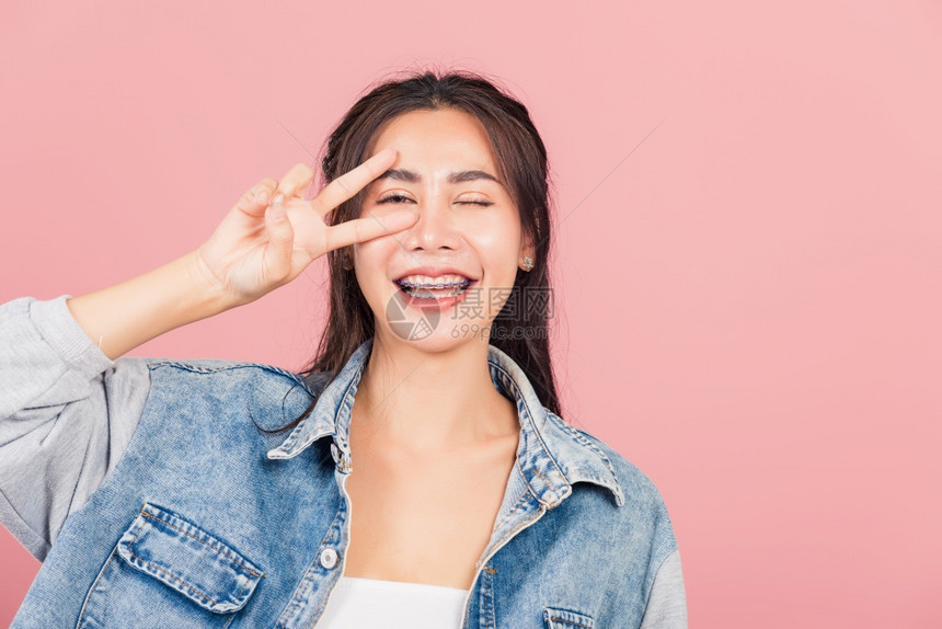 亚洲快乐的肖像美丽可爱的年轻女子戴尼姆微笑站着举起手指做VS胜利符号图片