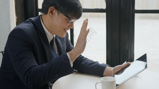 亚洲商人在咖啡店通过数码平板电脑的视频话微笑聊天图片