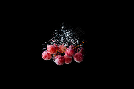 红葡萄沉在水中黑色背景与气泡背景图片