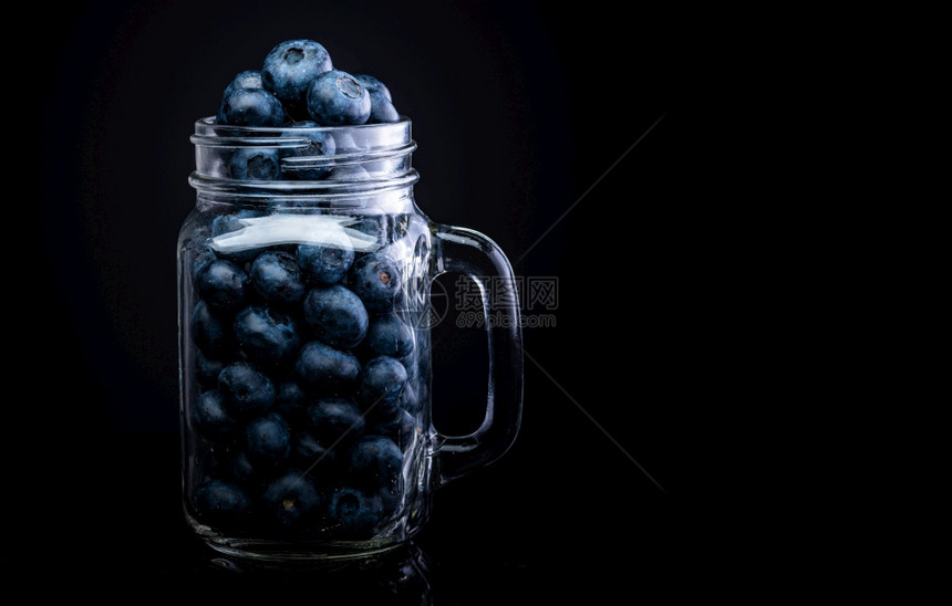 玻璃罐中的蓝莓与黑色背景隔绝复制空间在右边玻璃罐中的蓝莓与黑色背景隔绝图片