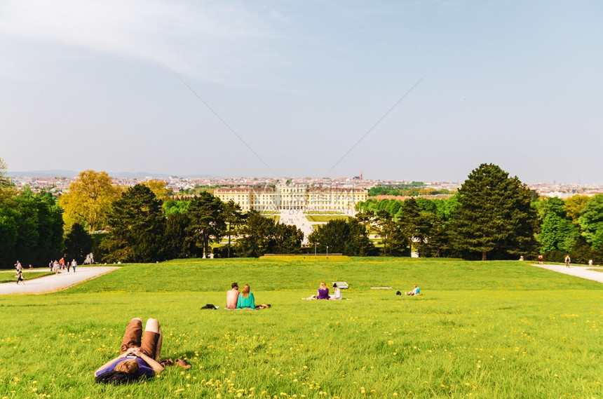维也纳奥地利2013年4月日从宫殿花园绿色山丘处前方的Schonbrunn宫殿景色享受草和湿润的人图片