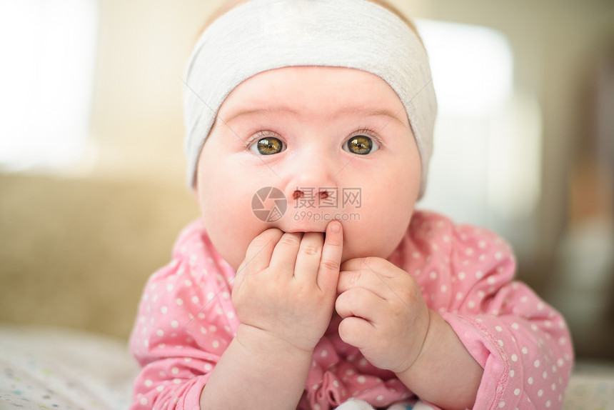 6个月大的女婴在肚子床上被切开头抬起来嘴中手指用大眼睛看着照相机6个月大的女婴在肚子上床被切开用大眼睛看着照相机图片
