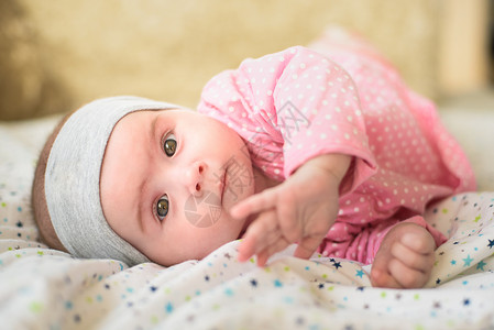 6个月大的女婴在肚子床上被切开6个月大的婴儿头抬起用大眼睛看镜头自然卧室灯光6个月大的女婴在肚子上床被切开6个月大的婴儿用眼睛看背景图片