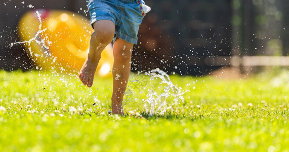 快乐的孩子在湿草坪上流水童年的概念图片