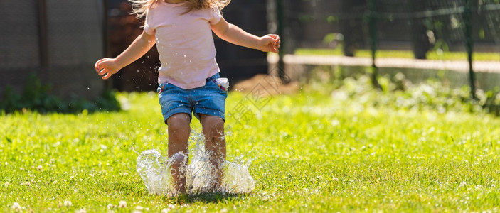 快乐的孩子在湿草坪上流水童年的概念图片
