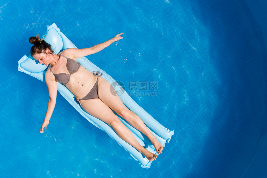 穿着比基尼的年轻女子在空中马特瑞斯环绕地面游泳池顶层风景家庭节日概念空中马特瑞斯的比基尼年轻女子在地面游泳池图片