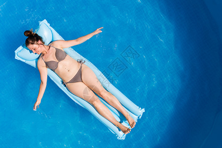 放松的救济穿着比基尼的年轻女子在空中马特瑞斯环绕地面游泳池顶层风景家庭节日概念空中马特瑞斯的比基尼年轻女子在地面游泳池背景