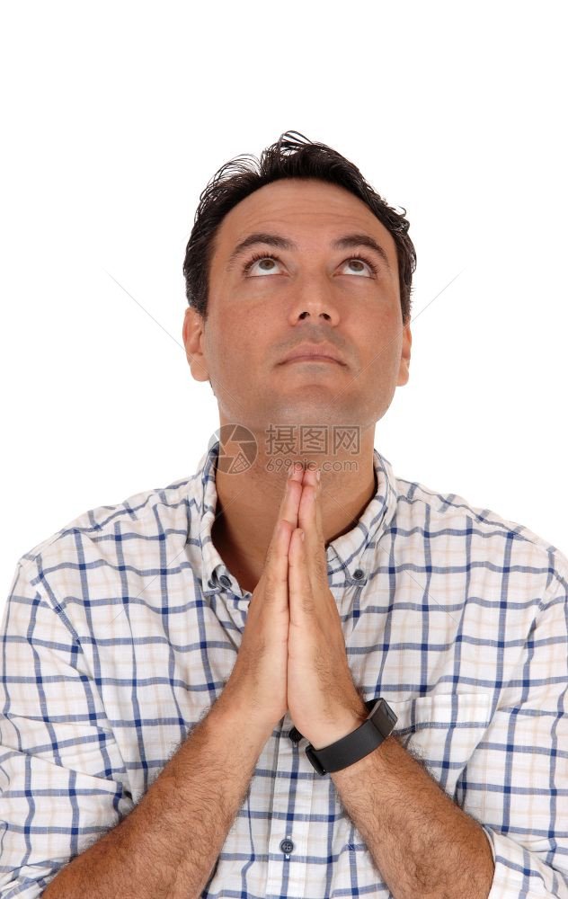 一个坐在椅子上折手的英俊男子仰望着向上帝祈祷为白种背景而孤立图片