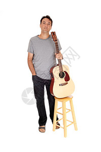 一个英俊的年轻男子在弹吉他后刹车站在牛仔灰色衬衫凉鞋与白色背景隔离图片