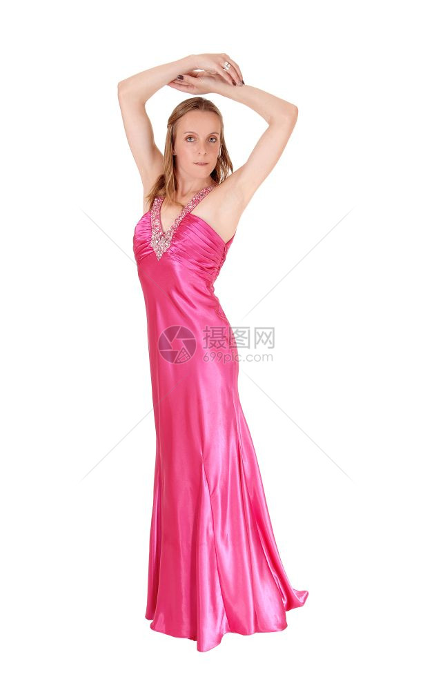 一个穿着长的粉红色晚礼服漂亮女人站在白背景与世隔绝的地方手放在头上图片