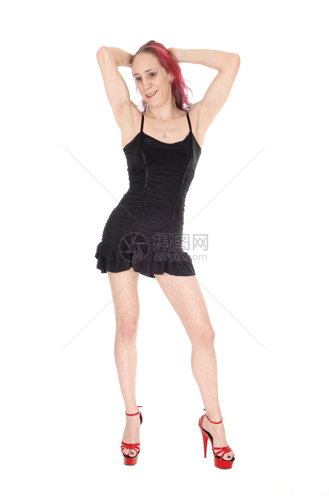 一位美丽的年轻女穿着黑色礼服从前面跳舞穿着红色高跟鞋举起手臂与白种背景隔绝图片