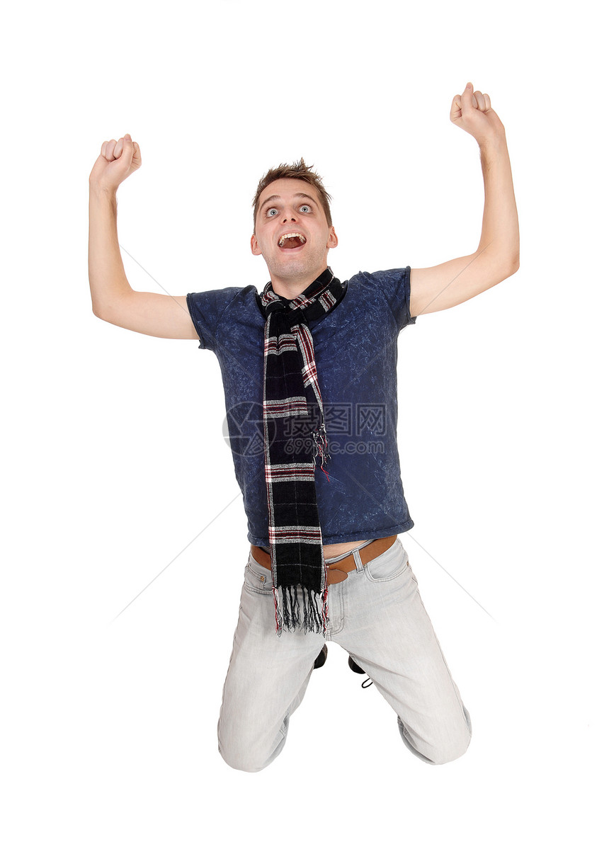 一个快乐的年轻男子跪在双膝上手伸入空气中尖叫穿着牛仔裤和围巾与白种背景隔绝图片