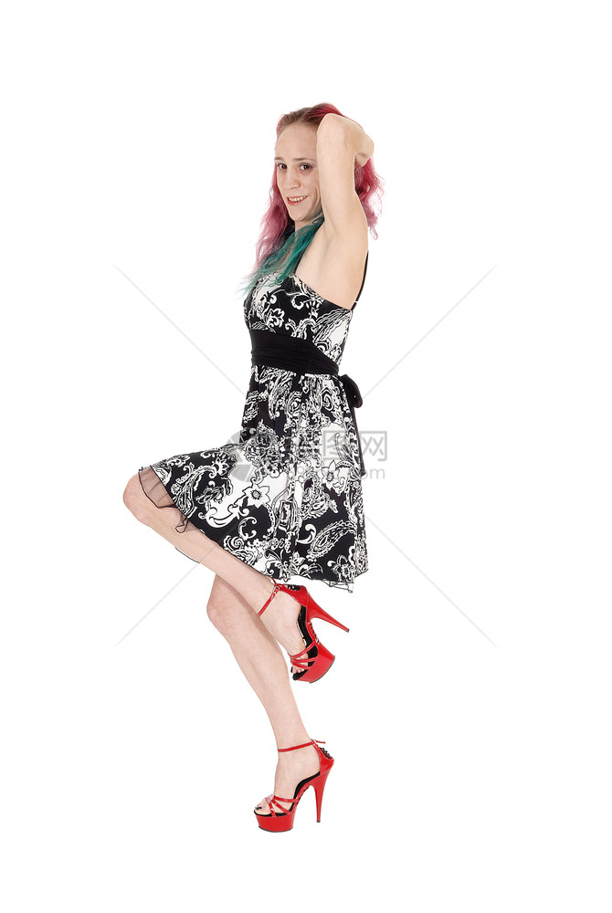 一个穿着短裙和红色高跟鞋的可爱年轻瘦女人一只腿抬起脚跳舞手放在头上被白背景隔离图片