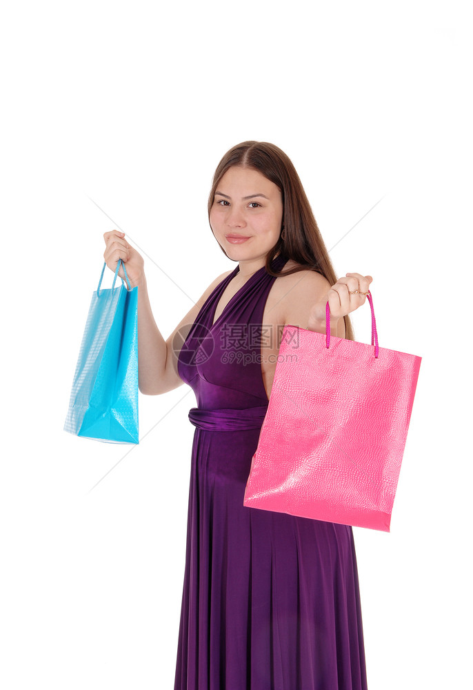 一个漂亮的年轻少女穿着勃根底礼服站在大学里举着两个购物袋与白种背景隔绝图片