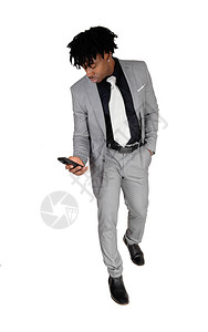 一个非裔美国人男子的全身照片着灰色轻光西装和黑衬衫看着他的手机图片