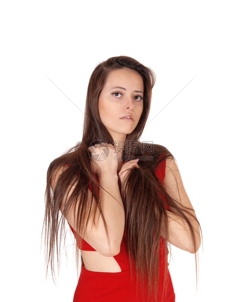 一位穿着红裙子的年轻美女肖像与她长褐发玩耍看着摄像机与白色背景隔绝图片
