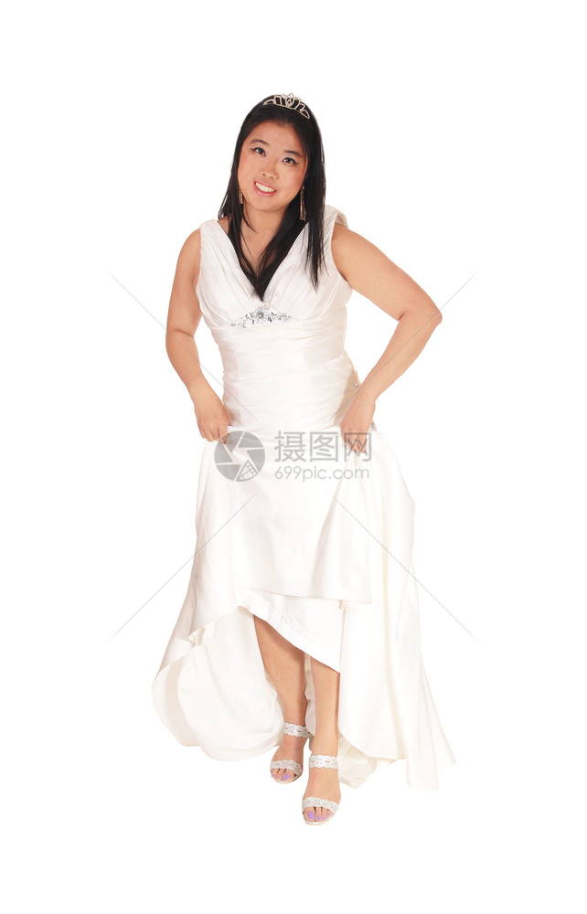 一个快乐笑的年轻新娘站在她的白色婚纱和长的黑头发举起她的裙子图片