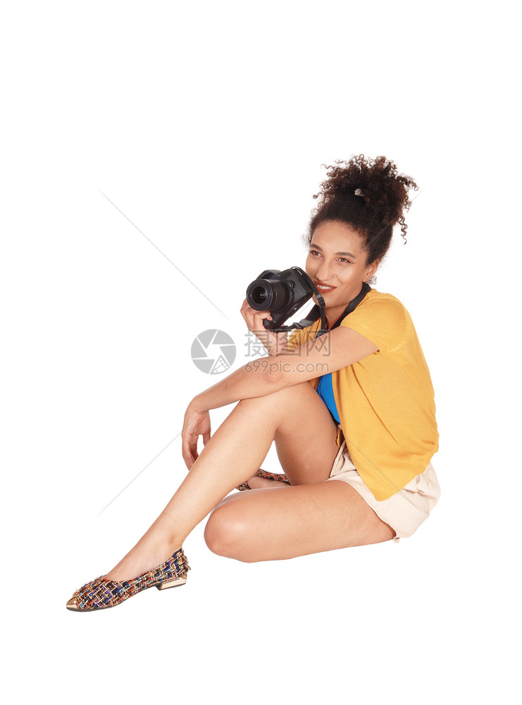 一名年轻的多种族妇女坐在地板上带着相机坐在地板上她的卷发黑色头看着摄影师因白背景被隔离图片