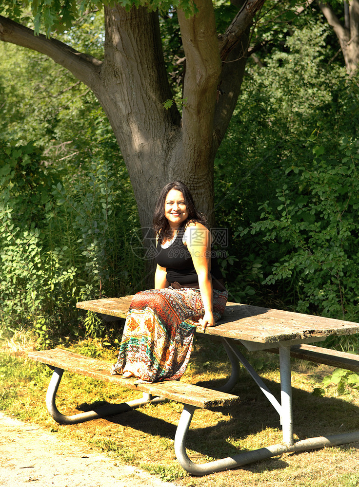 阳光明媚的一天坐在公园野餐桌上坐在边的年轻友善女人图片