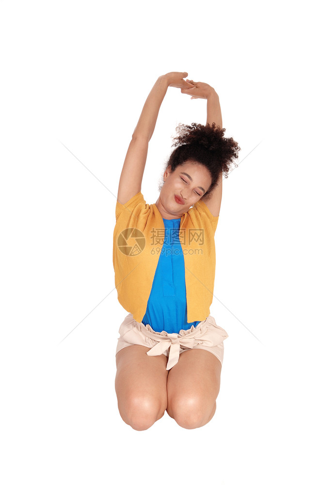 一个穿着短裤和毛衣的美丽多种族妇女跪在地上用闭着的眼睛伸展她双臂将其隔离在白地图片