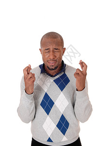 一个英俊的年轻非裔美国人男子站在他的手指交叉闭上眼睛着与白种背景隔绝图片