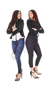 两个漂亮的年轻美女背靠站着穿牛仔裤和高跟鞋互相看着对方以白色背景隔离图片