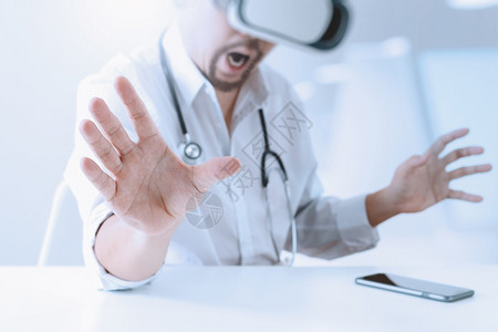 身戴虚拟现实镜的智能医生在现代办公室使用手机VR头盔图片