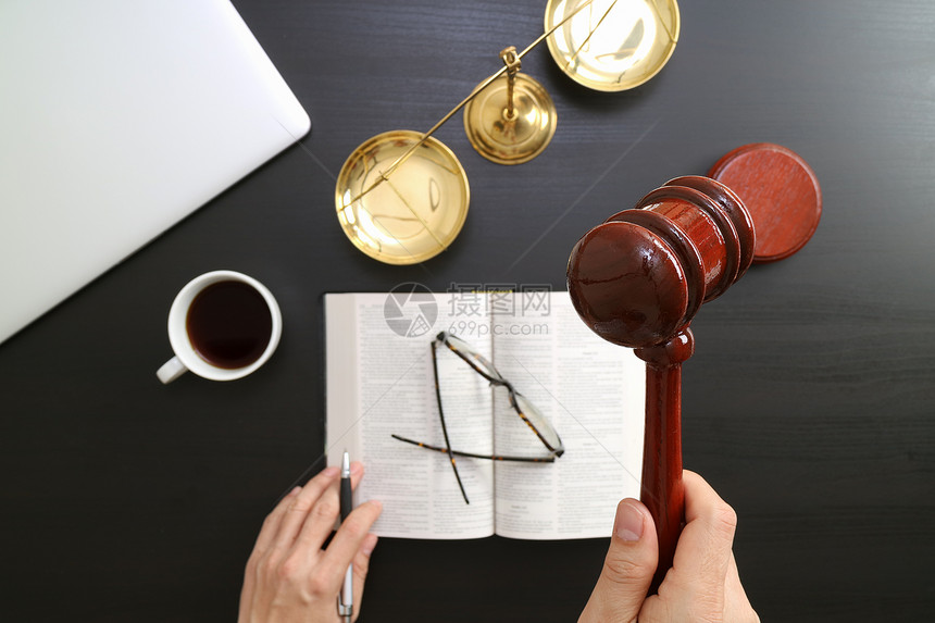 正义和法律概念男法官的TopViewofMaleJudge手放在法庭上持镯和黄铜电脑黑木桌上的公开圣经书图片