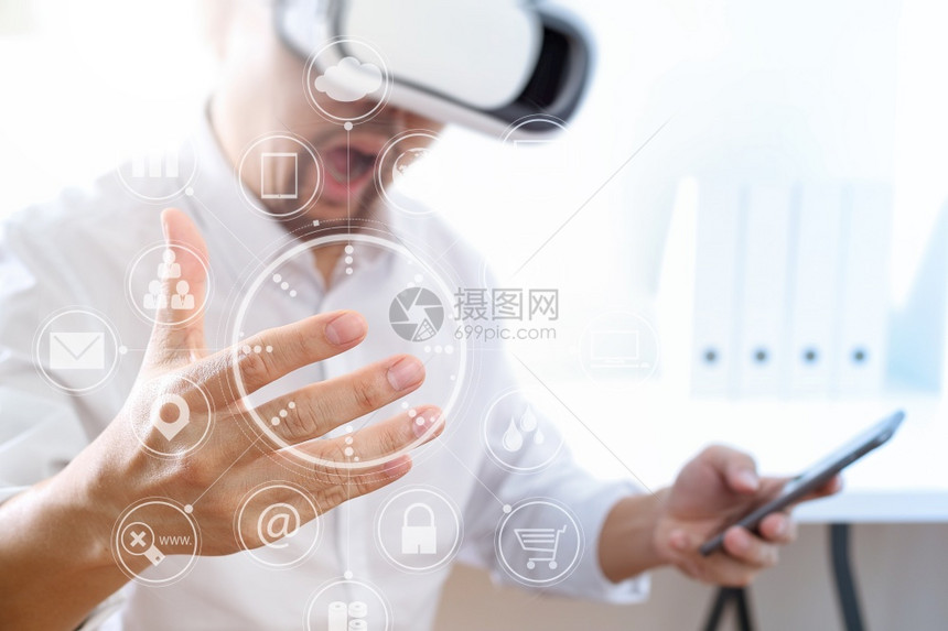 商人在现代办公室佩戴虚拟现实护目镜用手机使VR头戴带屏幕图标的VR头盔图片