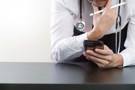 打电话的医生在暗木桌上用智能电话和听诊器工作设计图片