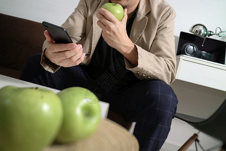 使用智能手机在线支付业务坐在客厅沙发上木盘中持绿苹果图片