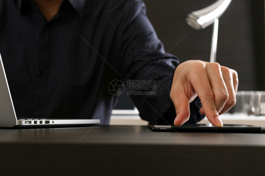 在现代办公室使用数字平板电脑和膝上型计算机及文件的商人图片