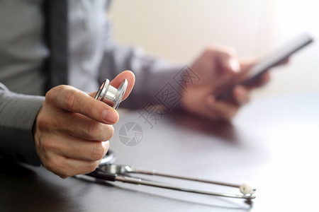 医生拿着手机在办公另一只手拿着听诊器图片