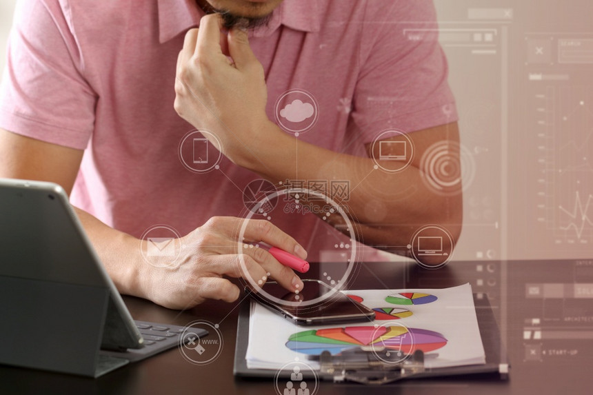使用智能电话和数字平板脑以及现代办公室木制桌文件的粉红色T恤衫商人与虚拟图标图片